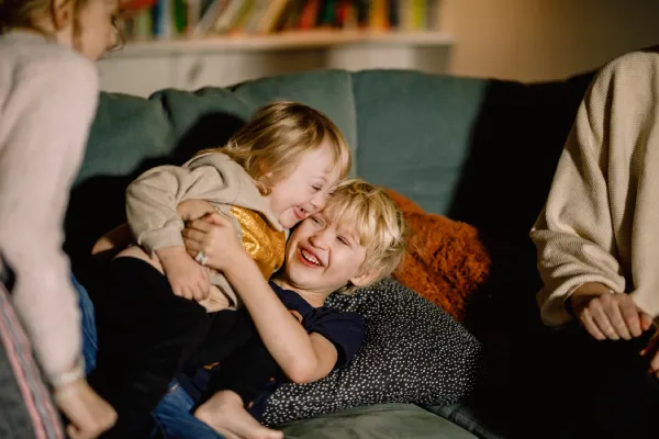 A child sits on a couch hugging a younger child, while their parents are partially visible on either side of the frame.