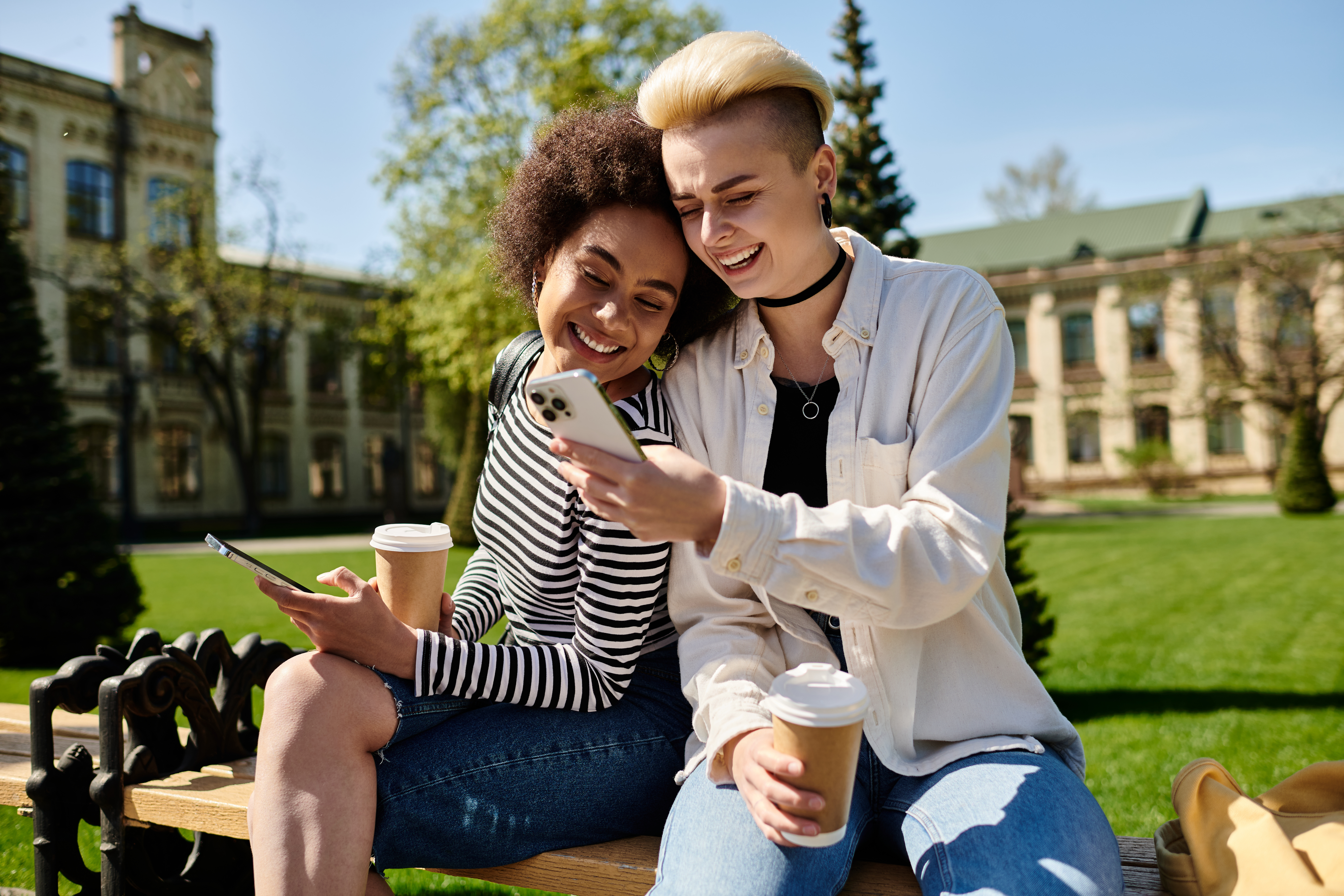 Two young women sitting on a bench, engrossed in their cell phones.