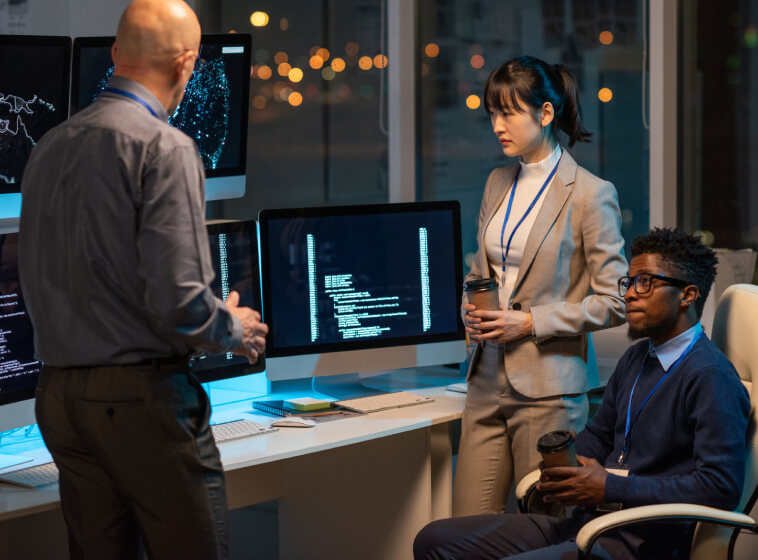 Three professionals in suits analysing data on computer screens in an office, representing cyber risk assessment.
