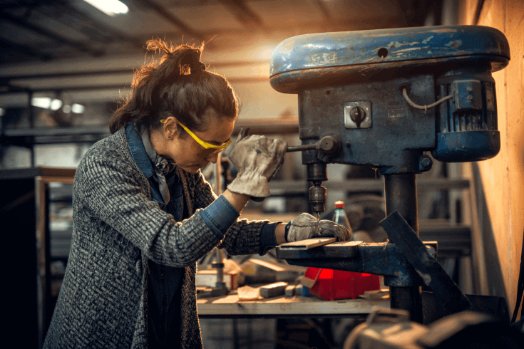 A tradesperson wears protective eyewear as they use a drill in their workshop