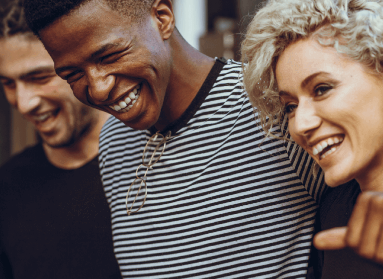 A trio of racially diverse young adults are looking into the distance and laughing. 