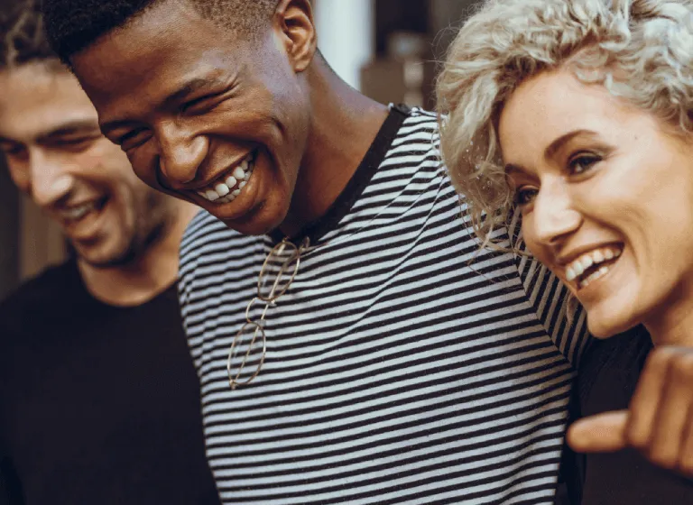 A trio of racially diverse young adults are looking into the distance and laughing.