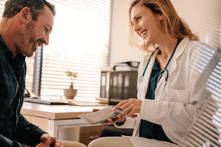 A female doctor shows information on digital tablet to a male patient while in a medical office.