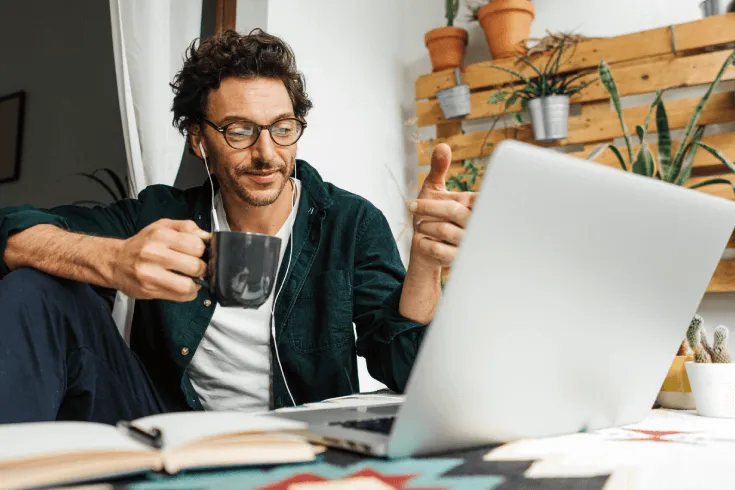 A man works from home on his laptop while drinking coffee.