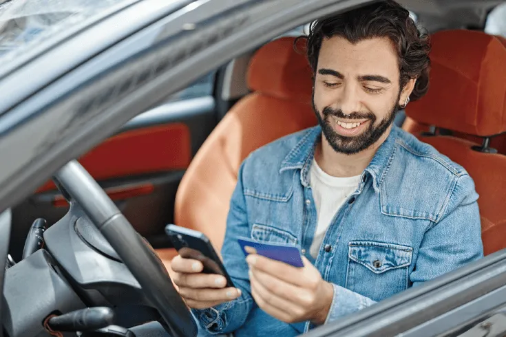 Person in car smiling at phone and bank card