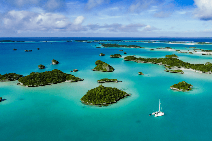 View of Fiji’s Fulaga Island. Image shows water full of various sized small islands with an anchored catamaran.