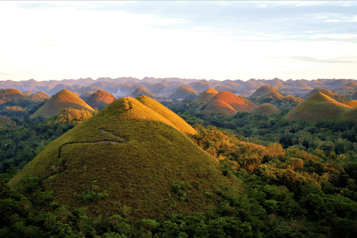 Chocolate hills in the Philippines. Bare mountain towering out of forest below with other bare hills poking out along the background.