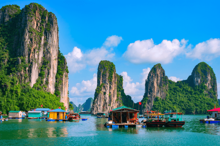 Alt text: Floating fishing village in Halong Bay with tall limestone cliffs in the background for a travel insurance Vietnam page