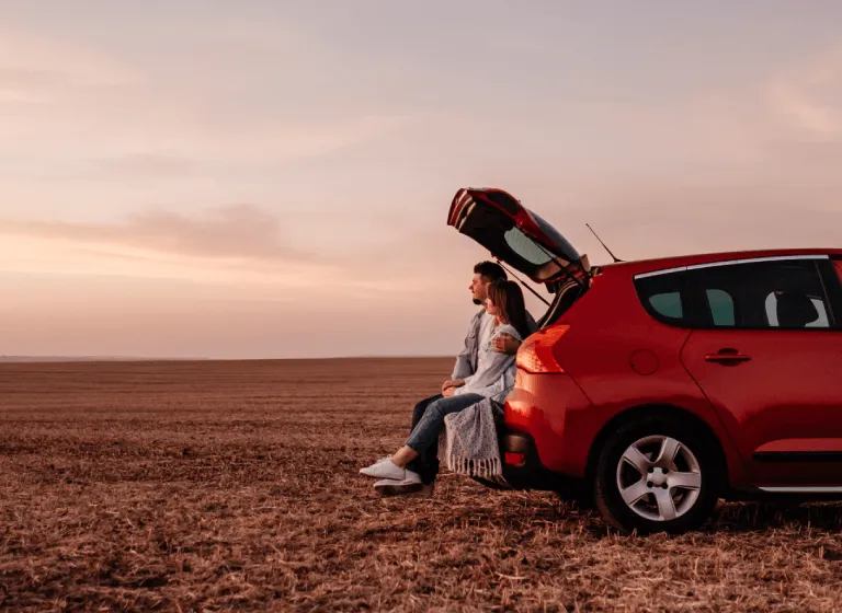 Tablet version of a couple sitting in car boot facing sunset on open field