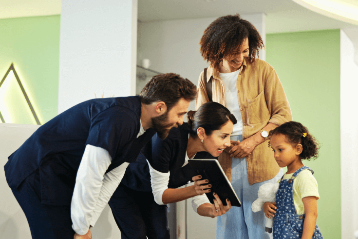Mother and young daughter standing with male and female nurse crouching down to the daughter with a tablet