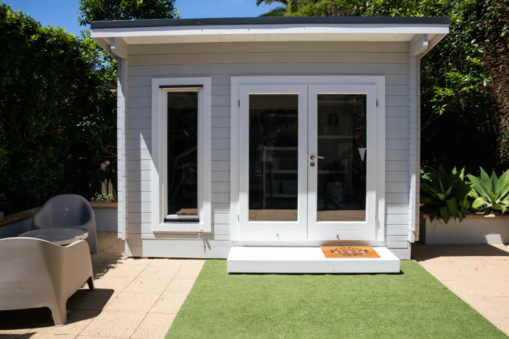 White and grey granny flat covered by granny flat insurance with a table, chairs, and grass set up in the backyard