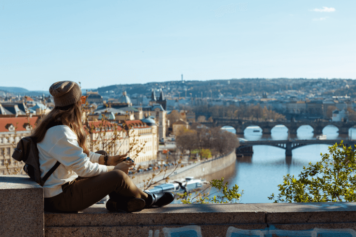 Woman sitting on stone railing overlooking city and river with bridges in the Czech Republic