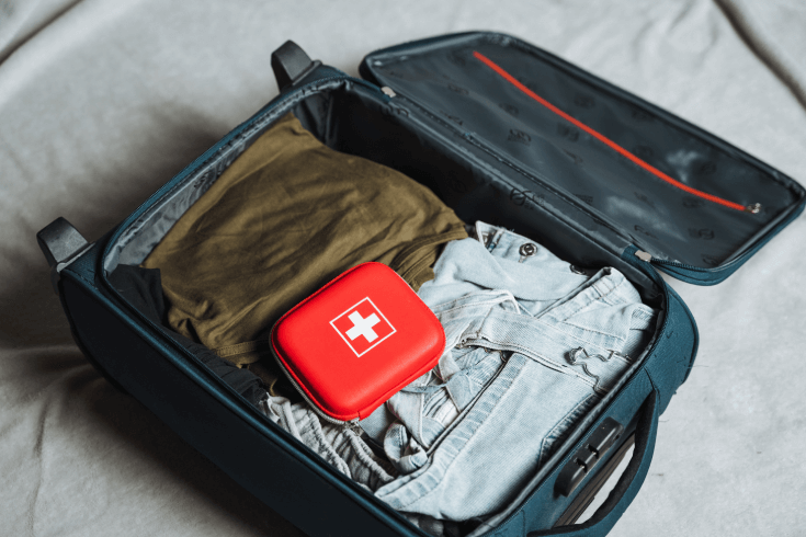 Open suitcase with clothes and red first aid kit inside
