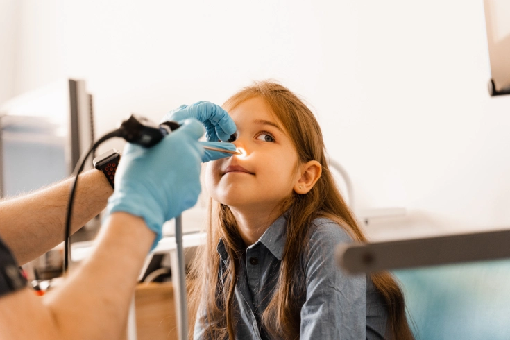 A young girl sits patiently as a doctor performs a nasal endoscopy