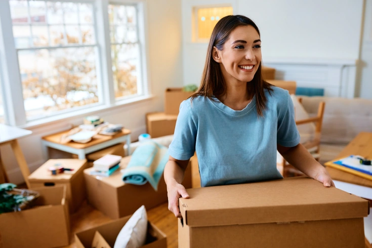 Young happy woman carrying a box and moving into her new apartment