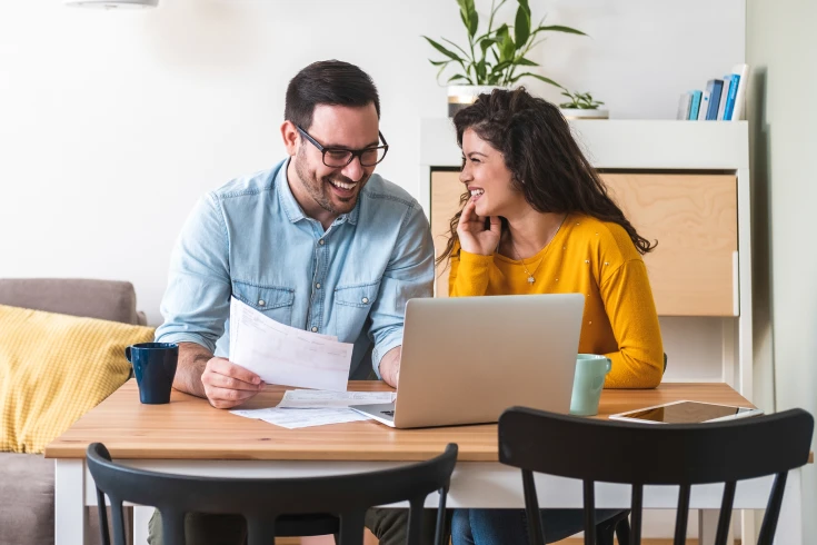 Couple happily crunching numbers with paperwork and a laptop to determine their borrowing power