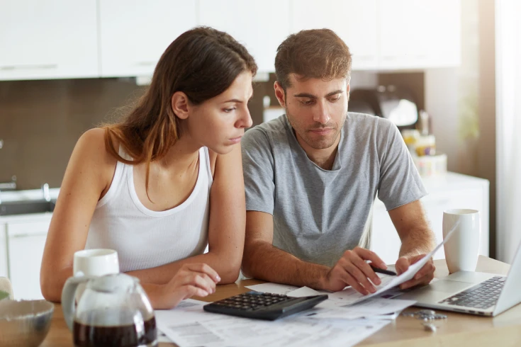 Couple crunching numbers while holding paperwork in the kitchen
