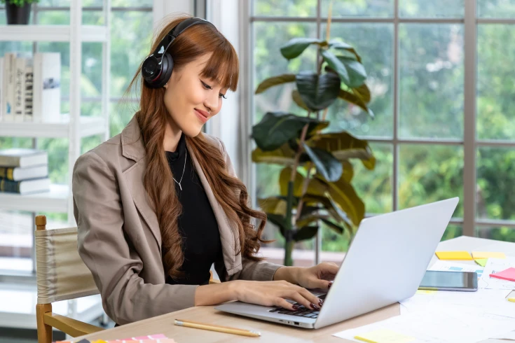 A woman wearing headphones types while looking at a computer monitor