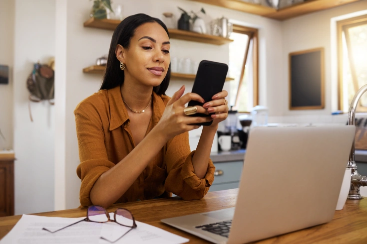 Person at desk looking at phone and laptop