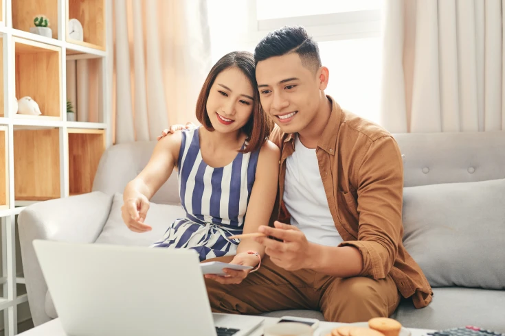 A couple sitting together on a couch at home, looking at a laptop screen.