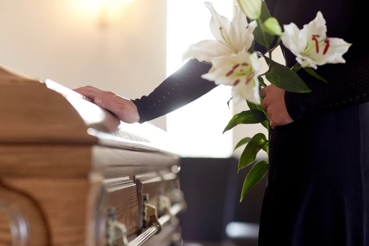 A person rests their hand on a loved one’s coffin at a funeral
