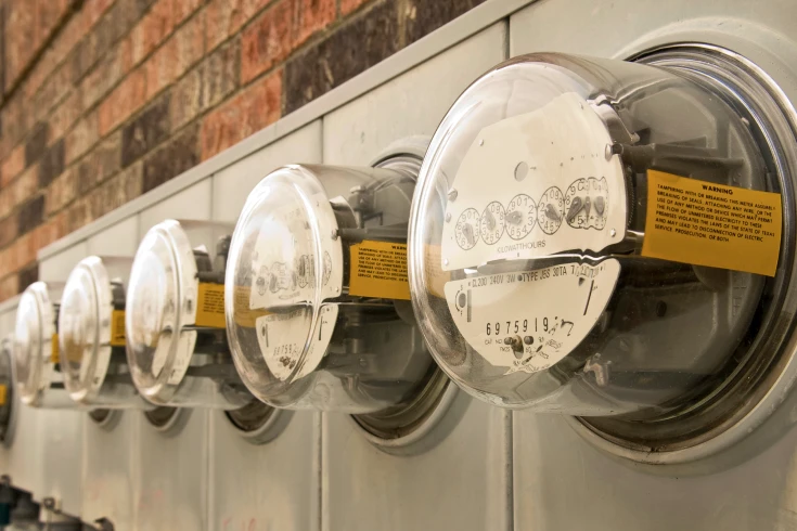 Five electricity meters lined up, all with a dial faces