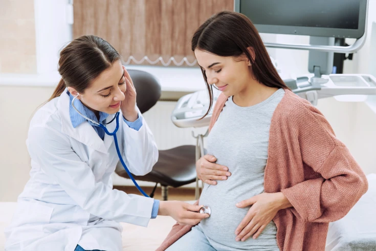 Female doctor checking pregnant woman’s belly with a stethoscope