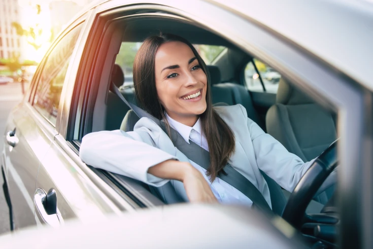 An image of a smiling woman in the driver's seat of a car