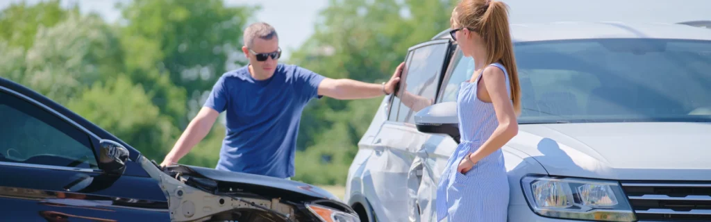 A male driver checks his car after a crash with a female driver.