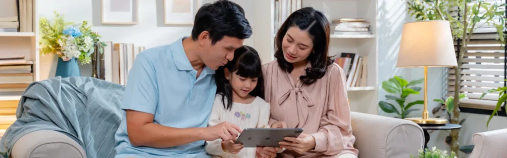 A father (left) and mother (right) chat to their daughter (middle) while looking at a tablet.