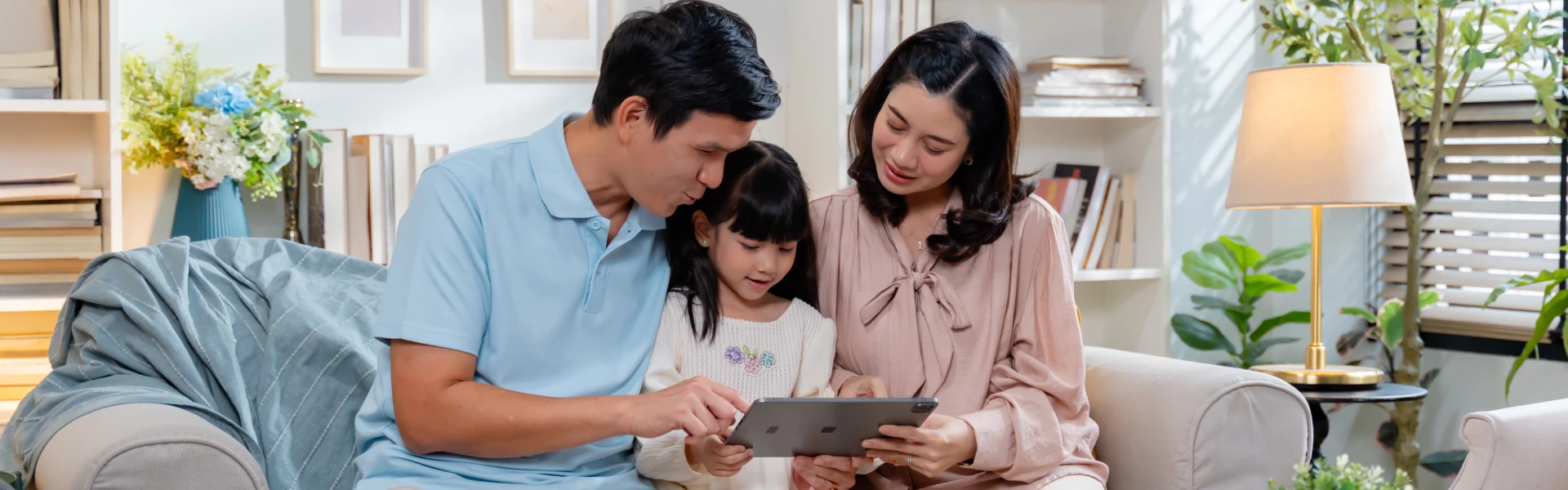 A father (left) and mother (right) chat to their daughter (middle) while looking at a tablet.