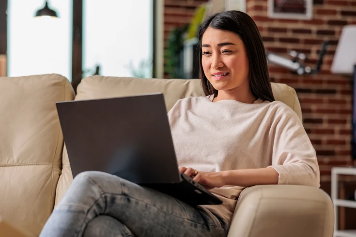 A woman sits on a couch and looks at a laptop