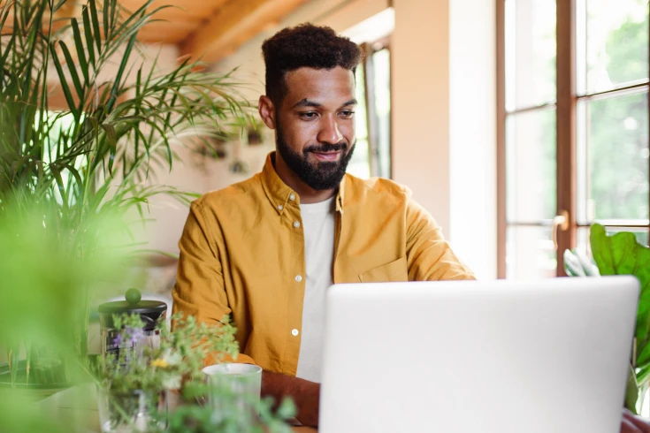 A man looks at a laptop, with plants behind him