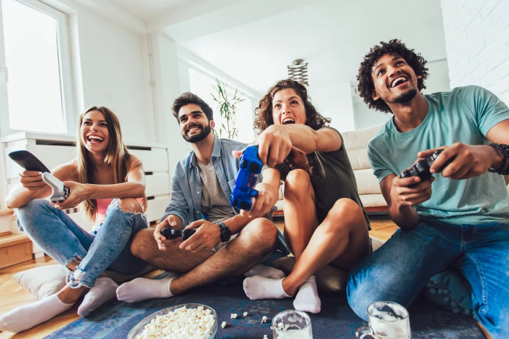 Four young people sit on the floor, playing a video game