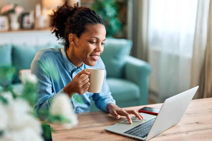A woman looks at a laptop and holds a coffee