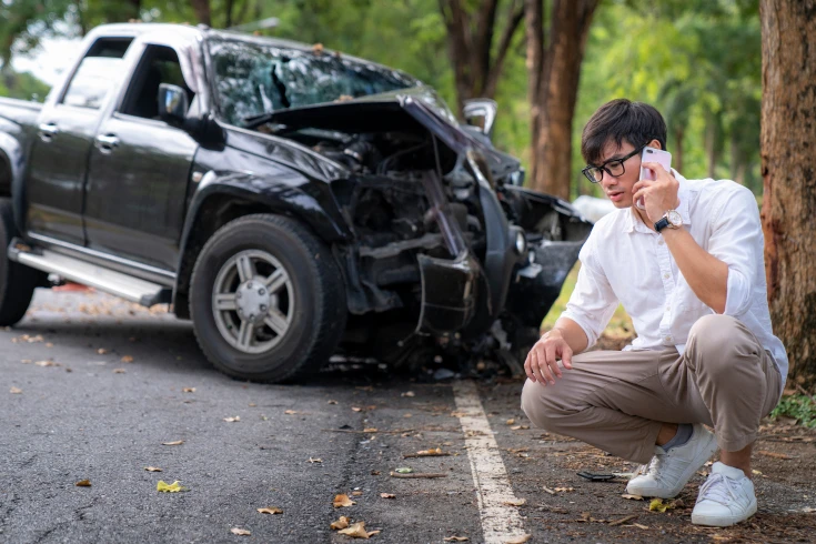Image of person on phone in front of a crashed car