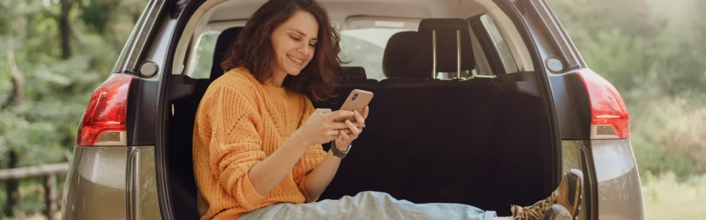 A female sits in the boot of her car looking at her mobile phone.