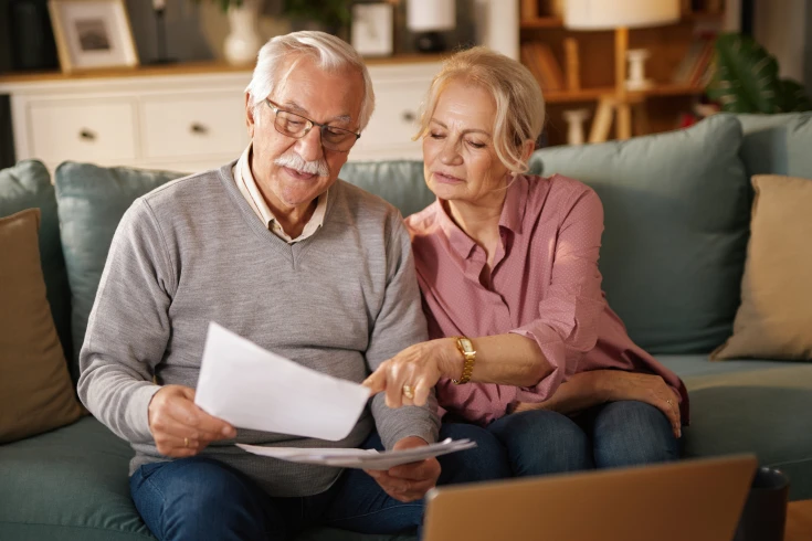 An older couple sit on a couch and look at a bill together