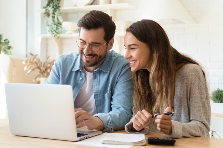 A man and woman sitting at a table in front of a laptop.