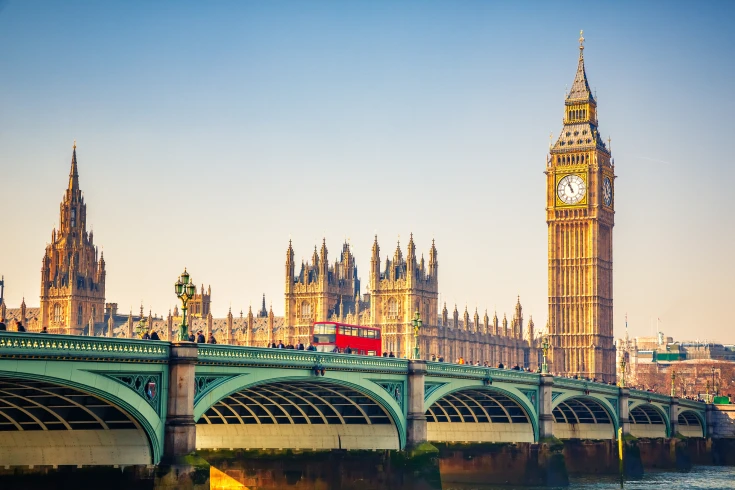 View of Big Ben and the bridge across the Thames, with a red double-decker bus driving across