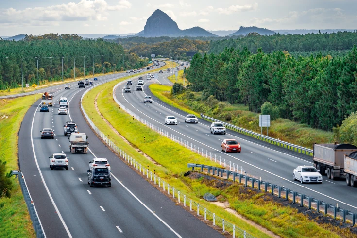 An image of a highway lined with trees and a scenery in the distance.