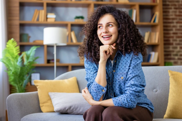 Woman sitting on couch inside with chin resting on hand
