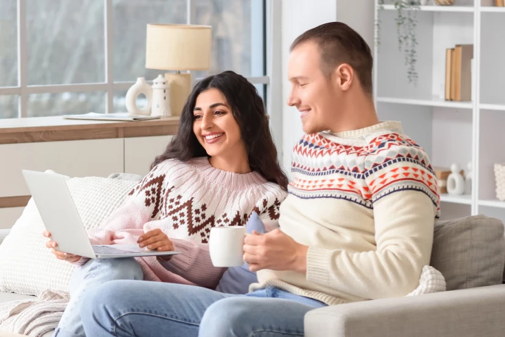 A man and woman sitting together on the couch looking at a laptop together