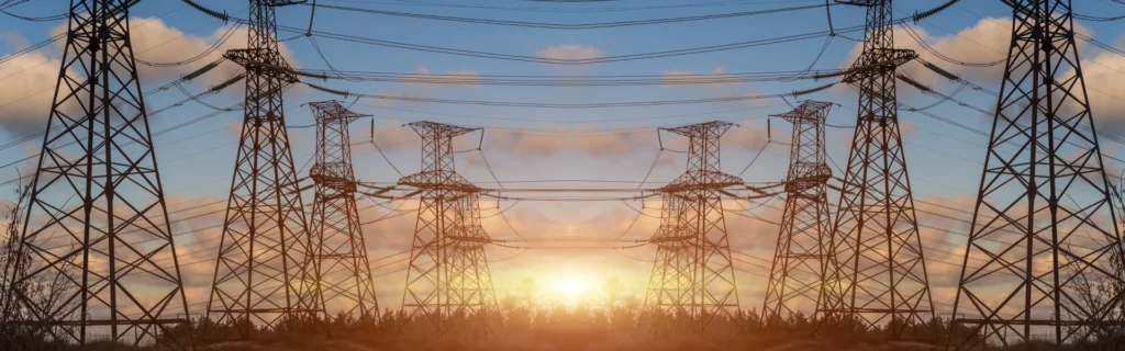 The sun sets in the background with powerline towers in the foreground.
