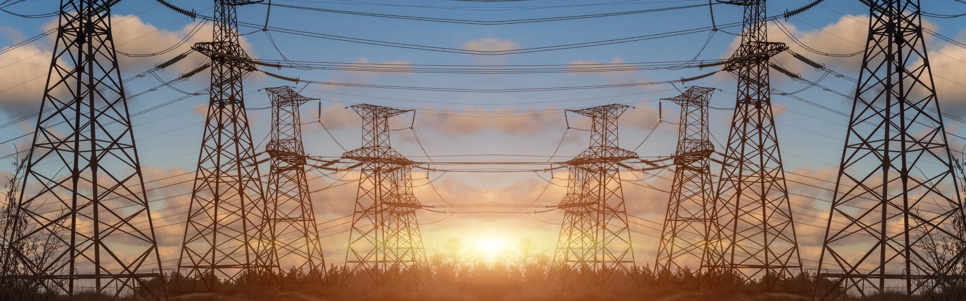 The sun sets in the background with powerline towers in the foreground.