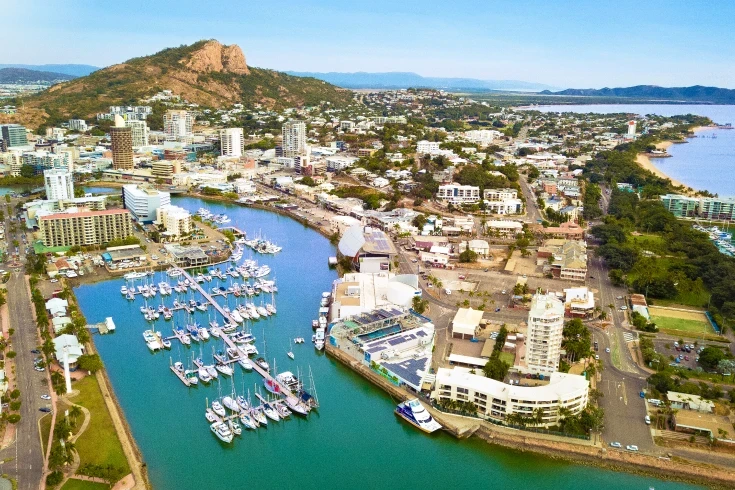 Aerial view of Queensland coastal town with river inlet docking area, mountaintop and coastline in background
