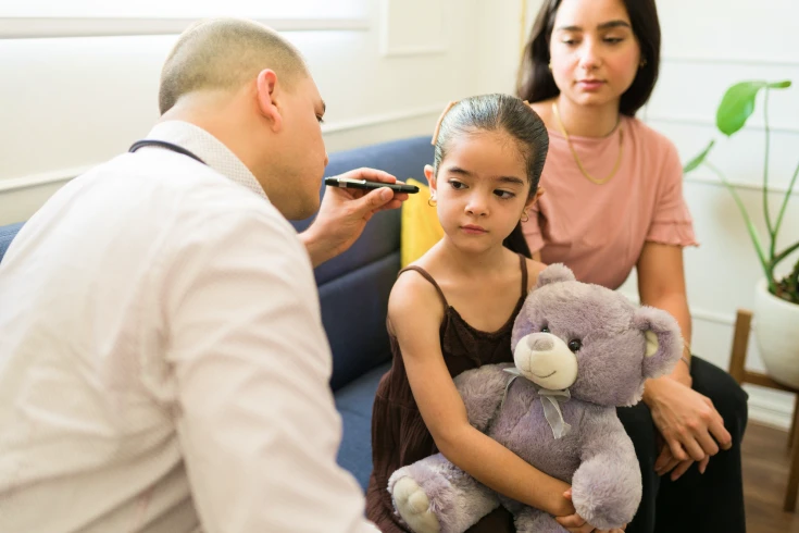ENT specialist having a look at a girl’s ear as her mother sits next to her