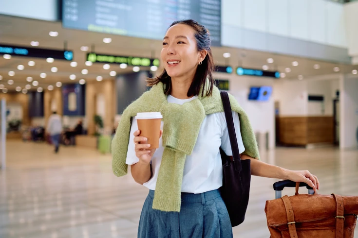 Woman at the airport, holding a coffee cup and suitcase