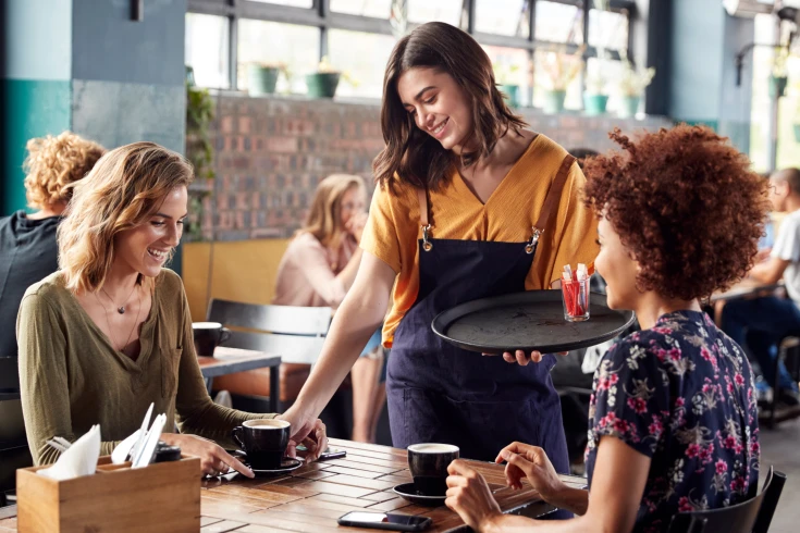 An image of a waiter serving two customers in a cafe