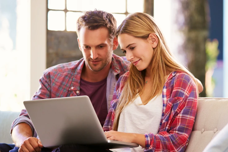 A couple sits on a couch and looks at a laptop screen